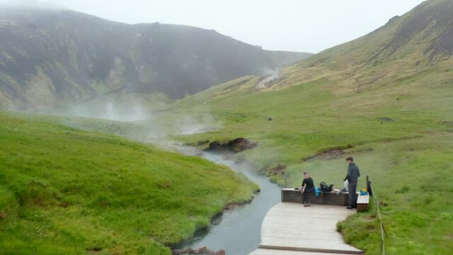 Drone view of Reykjadalur hot thermal river flowing through valley in Iceland. Aerial view of natural geothermal hot river stream in Reykjadalur Valley with wooden footpath and changing rooms