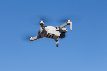 Gray unmanned aerial vehicle with four propellers and blades is flying on the blue sky background