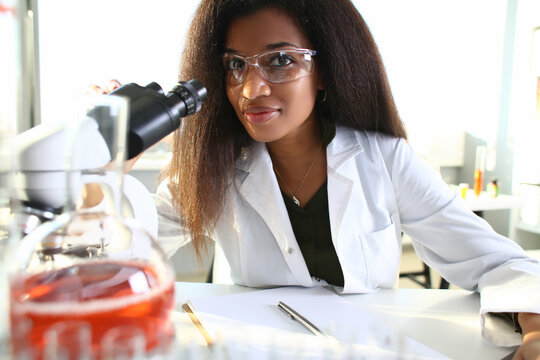 Black woman scientist in goggles, conducts study using microscope