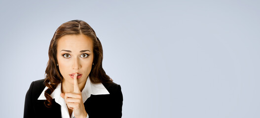 Portrait of young serious business woman keeping finger on her lips and asking to keep quiet,...