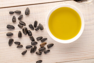 Many delicious sunflower seeds with a saucer of sunflower oil on a wooden table, close-up, top view.