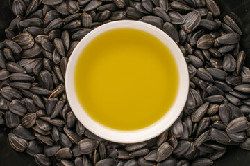 Many delicious sunflower seeds with a saucer of sunflower oil, close-up, top view.