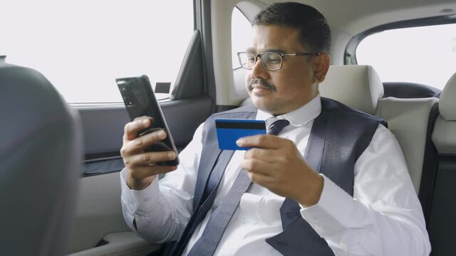 young indian businessman shopping online or paying bills on mobilephone by using credit card while traveling on taxi car - concept of digital payment and e-commerce shopping.