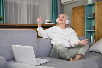 elderly woman in headphones listens to music and dances at home in the evening. seniors llifestyle
