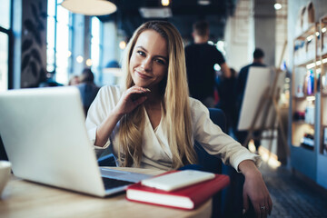 Young happy woman touching chin at table with laptop