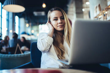 Positive young businesswoman working remotely on laptop in cafe