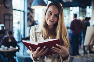 Young happy woman reading book in cafe