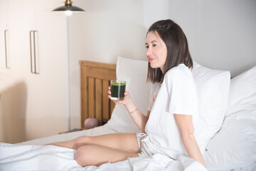 Obraz na płótnie Canvas woman drinks green smoothie sitting on bed. healthy food. Nutrition concept.
