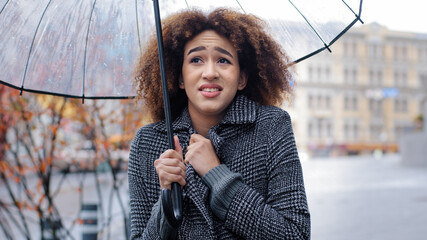 African American girl curly-haired sad woman in stylish coat stands in autumn on city street with...
