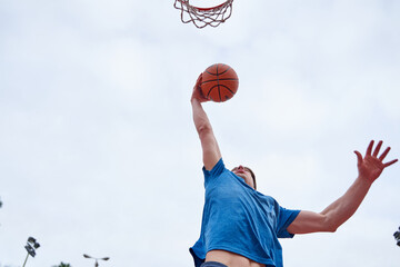young Caucasian man dunking on an outdoor basketball court. concept of sport