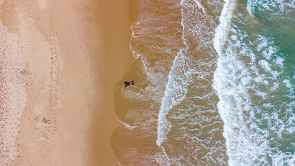homem deitado na areia com ondas visto de drone - obrazy, fototapety, plakaty