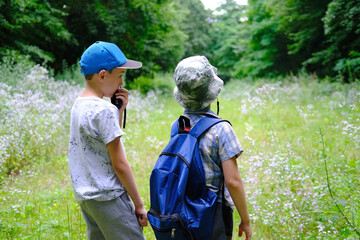 two children 7-9 years old with a backpack, boys talking on a walkie-talkie in the forest, the...