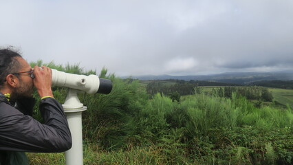 A male person is looking to the future with a white telescope, binoculars view to green landscape on a cloudy day in Nordspanien