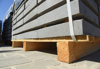 Concrete tiles for the construction of a pedestrian road are laid on a new wooden pallet, close-up.