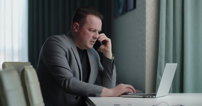 serious man working on laptop and talking on mobile phone