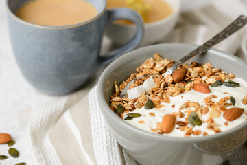 Concept of breakfast with granola muesli, yogurt, pumpkin seeds, almonds and coconut pieces in boul with a spoon on the light table. Selective focus, low depth of field