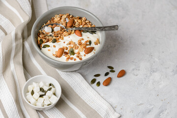 Concept of breakfast with granola muesli, yogurt, pumpkin seeds, almonds and coconut pieces in bouls with a spoon on the light table.