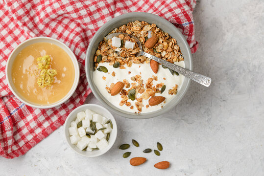 Cooked granola muesli with yogurt, honey, pumpkin seeds, almonds and coconut pieces in bouls with a spoon on the light table. Flat lay of breakfast, top view