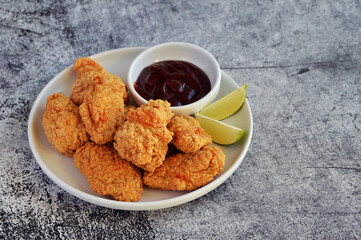 Crispy fried chicken served with BBQ sauce and lime wedges on the side in rustic background