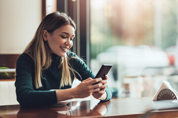 Young happy woman at restaurant drinking coffee and using mobile phone.
