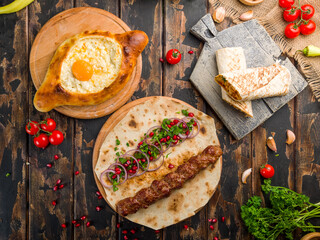 ajara Khachapuri with cheese, egg and butter, lula kebab with lamb, shawarma with chicken, georgian kitchen on wooden table top view