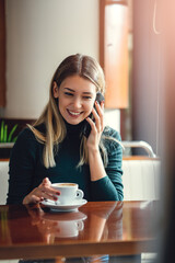 Young happy woman at restaurant drinking coffee and using mobile phone.