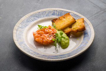 salmon Tartar on a plate with mashed avocado on grey concrete table