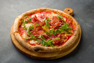 Pizza with Parma ham and arugula on the board on grey concrete table
