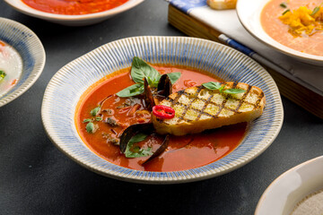 tomato soup with mussels and fried bread on grey concrete table