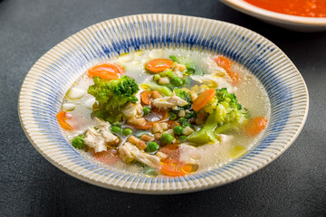 Chicken soup bouillon in a plate with vegetables on grey concrete table macro close up