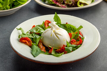 Salad with buratta cheese, sun dried tomatoes and greens on grey concrete table
