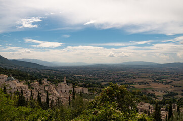 Fototapeta na wymiar Foto di panorama da Assisi, Umbria, Italia dalla rocca medievale in cima alla collina, scattata dall'alto in una giornata di sole con nuvole diffuse e veduta sulla vallata umbra.