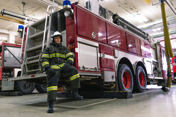 A firefighter in special clothes is sitting on the running board of a fire truck. A fire truck at the fire station. Rescue service.