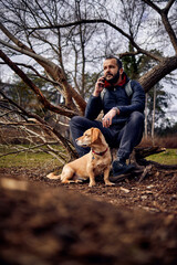 a handsome bearded man sitting in a park with his dog