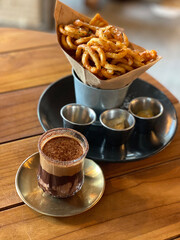 The vertical curly crispy French fries inside bucket with sauce and glass of cold dirty mocha...