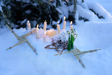 Wiccan altar for Imbolc sabbath, pagan holiday ritual. Brigid's cross of straw, candles, snowdrops, toy sheep on snow, winter forest natural background. symbol of Imbolc holiday, spring equinox. - obrazy, fototapety, plakaty
