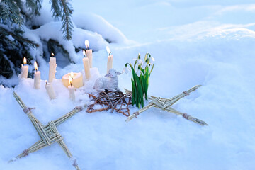 Wiccan altar for Imbolc sabbath, pagan holiday ritual. Brigid's cross of straw, candles, snowdrops, toy sheep on snow, winter forest natural background. symbol of Imbolc holiday, spring equinox. - obrazy, fototapety, plakaty