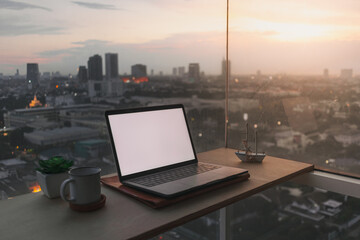 Fototapeta na wymiar Laptop on wooden desk at the balcony with evening sunset city view.