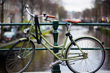Fototapeta na wymiar Rainy day in Amsterdam. Bicycle on wet street in Amsterdam in rain. Bike over canal. Picturesque town landscape in Netherlands. Toned photo.