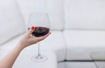 A woman's hand holds a glass of red wine at home. Selective focus.