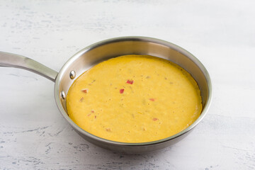 Vegan chickpea omelette in frying pan, cooking on a light gray textured background. Healthy...