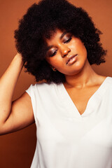 pretty young african american woman with curly hair posing cheerful gesturing on brown background, lifestyle people concept