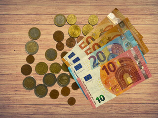 Euro currency note bills and coins scattered around - top view flat lay on wooden texture background.