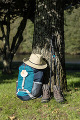 Backpack of a pilgrim leaning against a tree with a hat, trekking boots and poles in a wooded area....