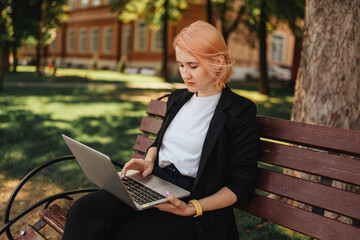 Pretty young caucasian woman go for a walk at park with coffe and laptop. Working outdoors