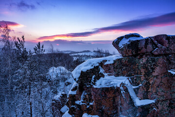 Rock, winter forest and village at sunset