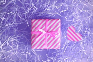 Gift with pink ribbon ribbon on a background with a Very Peri color paper filler. The tradition of...
