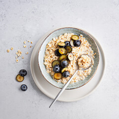 Oatmeal porridge with blueberries, honey in bowl on light surface background. Healthy food for breakfast.