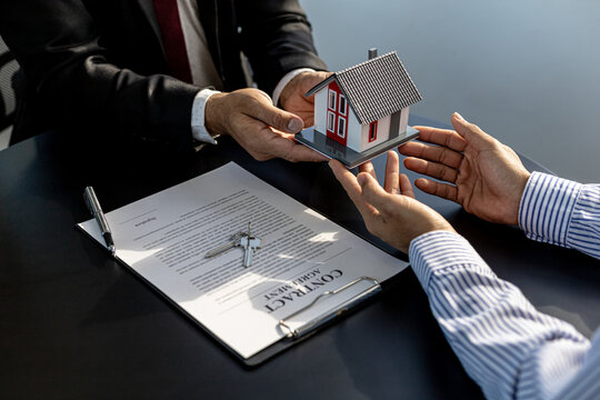 Two people holding a small model house, the home salesman handing over the house to the customer after signing the contract and inspecting the house. Real estate trading ideas.