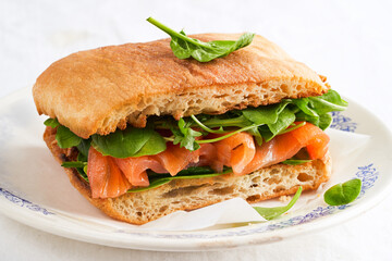 Delicious brunch, breakfast - sandwich with smoked salmon and fresh spinach, arugula leaves, on a light background.